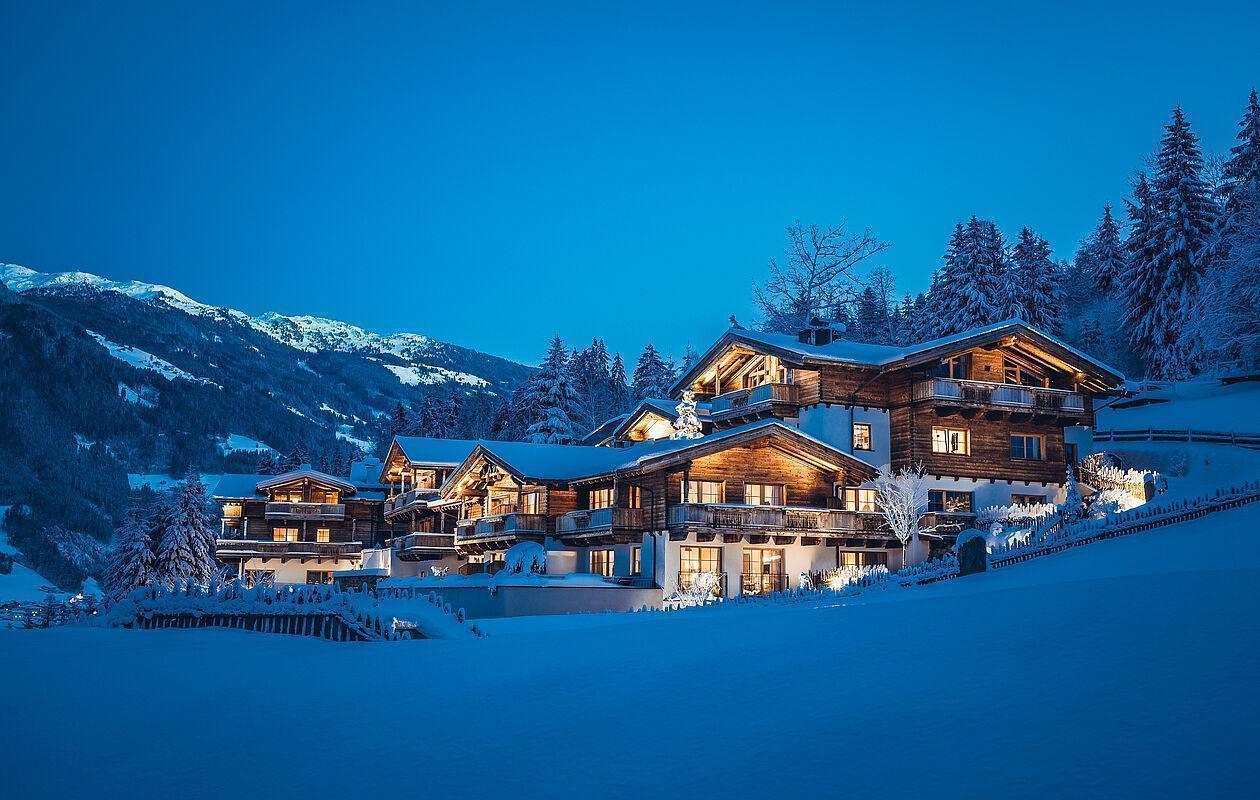 Das beleuchtete Naturhotel Kaltenbach im Zillertal bei Nacht umgeben von schneebedeckten Bergen 