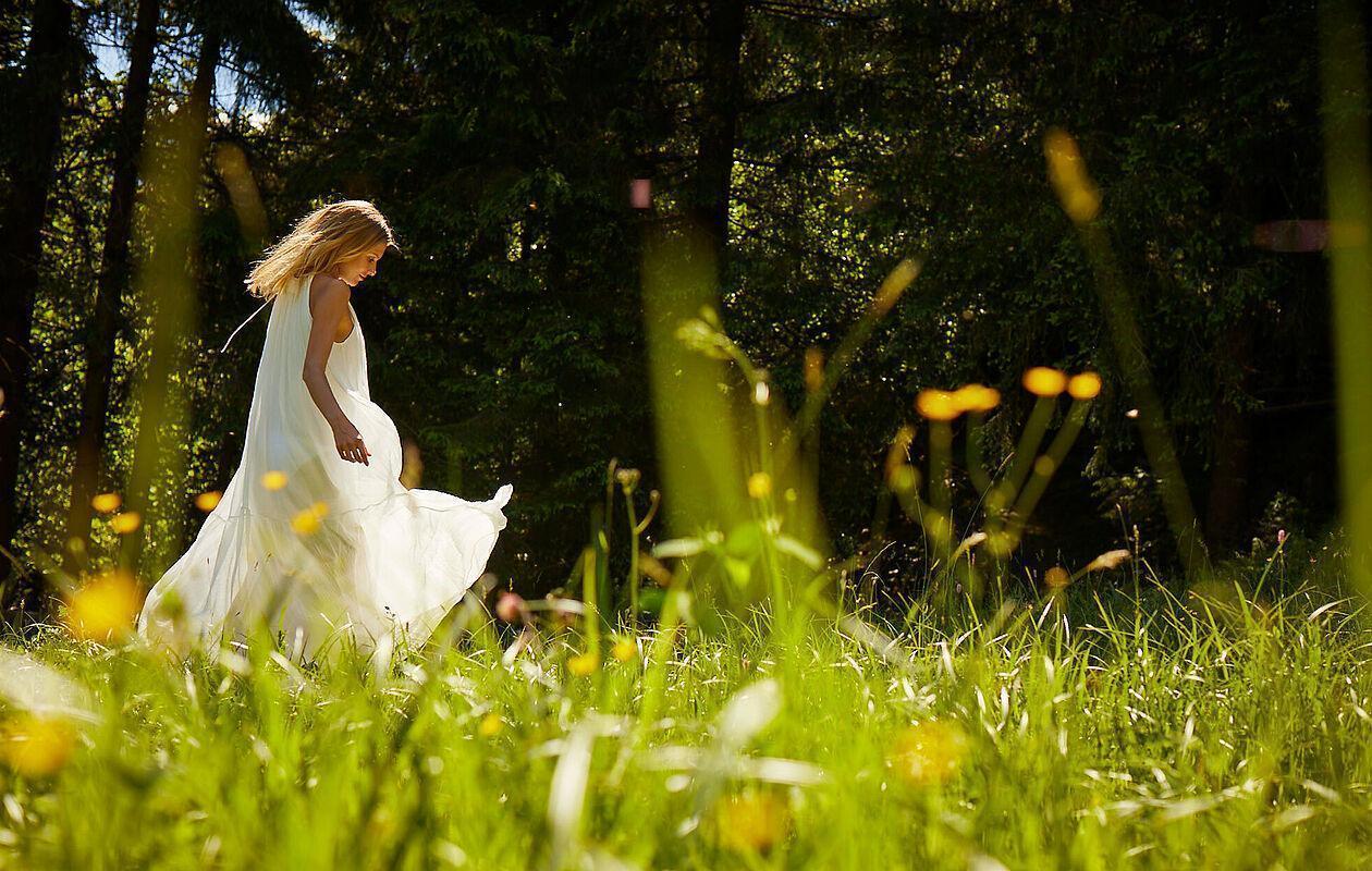 Eine junge Dame spaziert im langen weißen Kleid über eine grüne Frühlingswiese in der Nähe des Hotel Kaltenbach