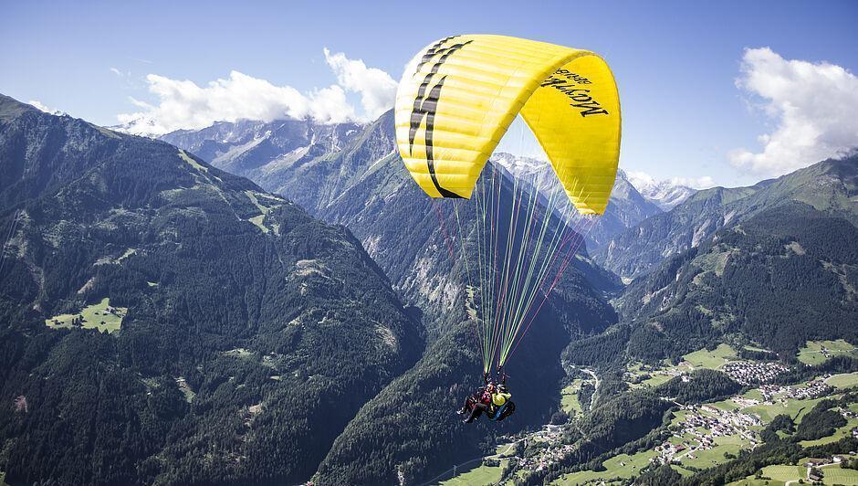 Ein Gast genießt seinen Sommerurlaub in Tirol beim Paragliding über einem Tal