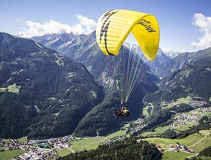 Ein Gast genießt seinen Sommerurlaub in Tirol beim Paragliding über einem Tal