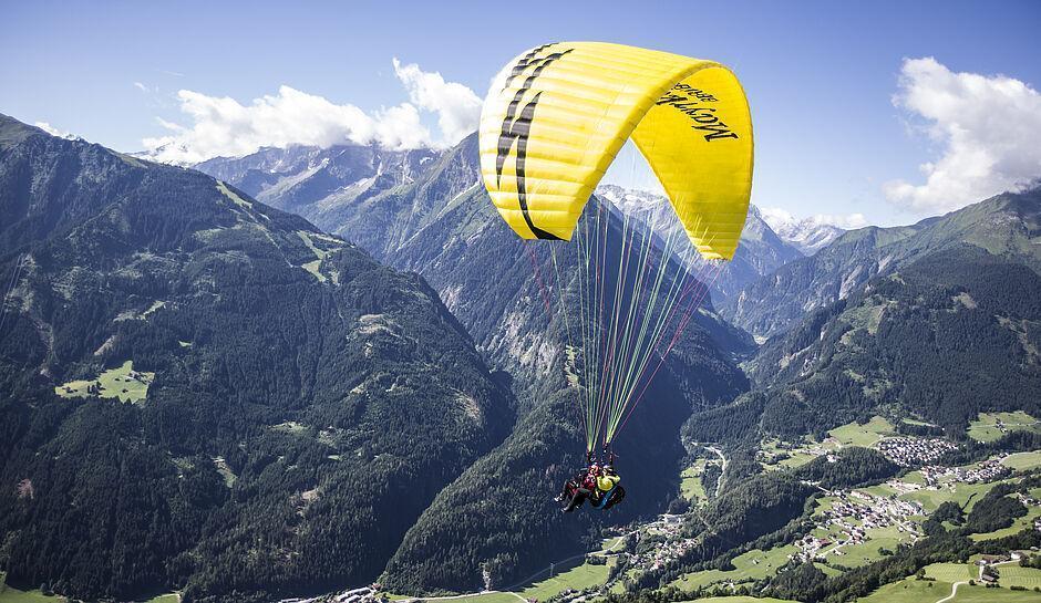 Ein Gast genießt seinen Sommerurlaub in Tirol beim Paragliding über einem Tal