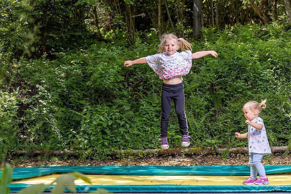 Zwei kleine Mädchen hüpfen im Park auf einem großen gelben Trampolin 
