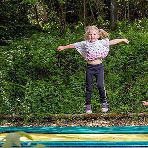 Zwei kleine Mädchen hüpfen im Park auf einem großen gelben Trampolin 