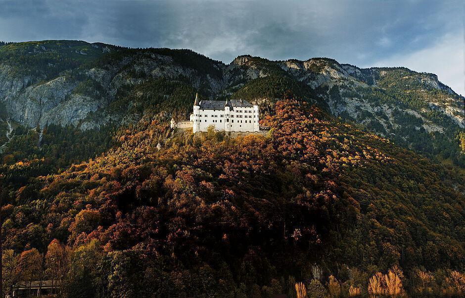 Außenansicht des Schloss Tratzberg vor Bergkulisse, herbstlichen Bäumen und blauem Himmel