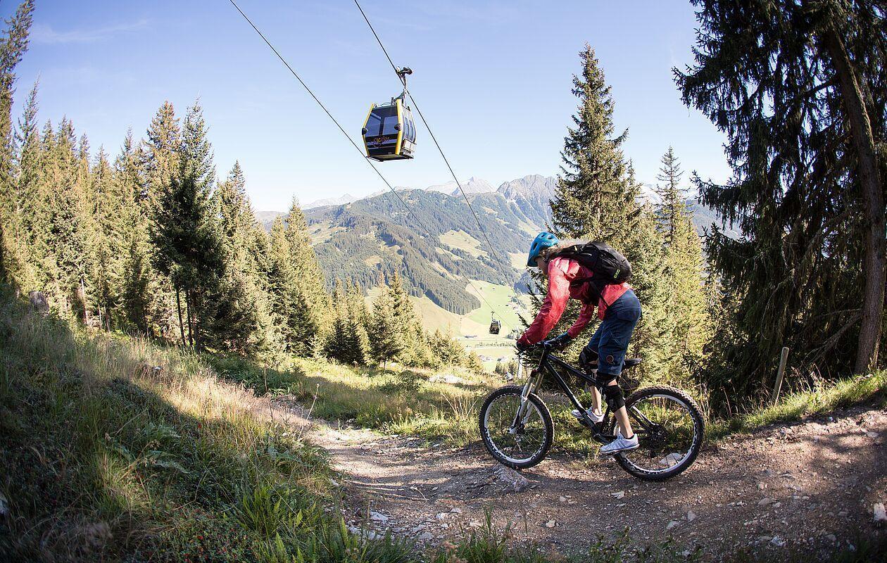 Eine Mountainbikerin fährt auf einem Pfad unter der Bergbahn