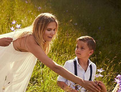 Mutter und Sohn pflücken lila Blumen auf einer grünen Wiese in Tirol 