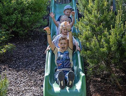 Vier Kinder rutschen auf einer grünen Rutsche im Familienhotel Tirol