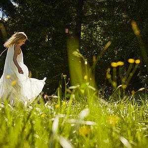 Dame in weißem Kleid tanzt fröhlich über eine Blumenwiese in den Bergen 
