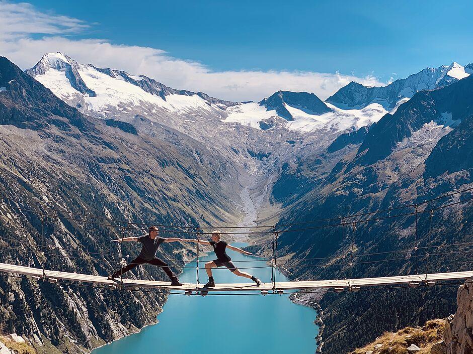 Zwei Männer machen Yoga auf einer Hängebrücke in den Bergen von Österreich 