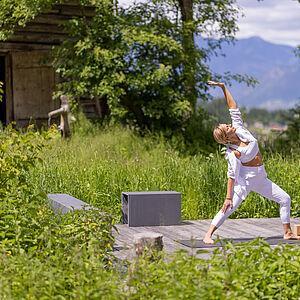 Hotelgast macht auf einem Holzsteg in der Natur eine Yogaeinheit 