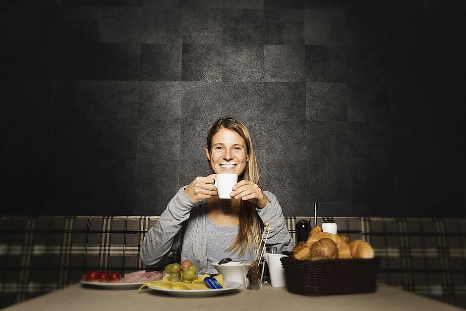 Eine Frau lächelt mit Tasse in der Hand und Milchbart, während sie vor dem Vital Frühstück im Das Kaltenbach sitzt