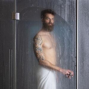 Hotelgast steht im Wellnessbereich des Hotels in einer gläsernen Dusche 