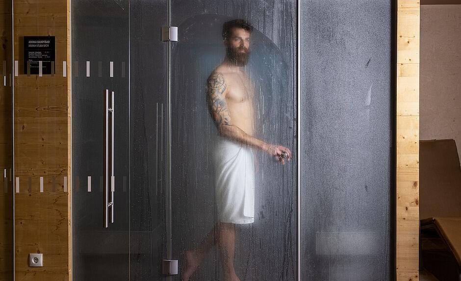 Gast mit Handtuch steht in einer Dusche im Wellnessbereich des Hotels