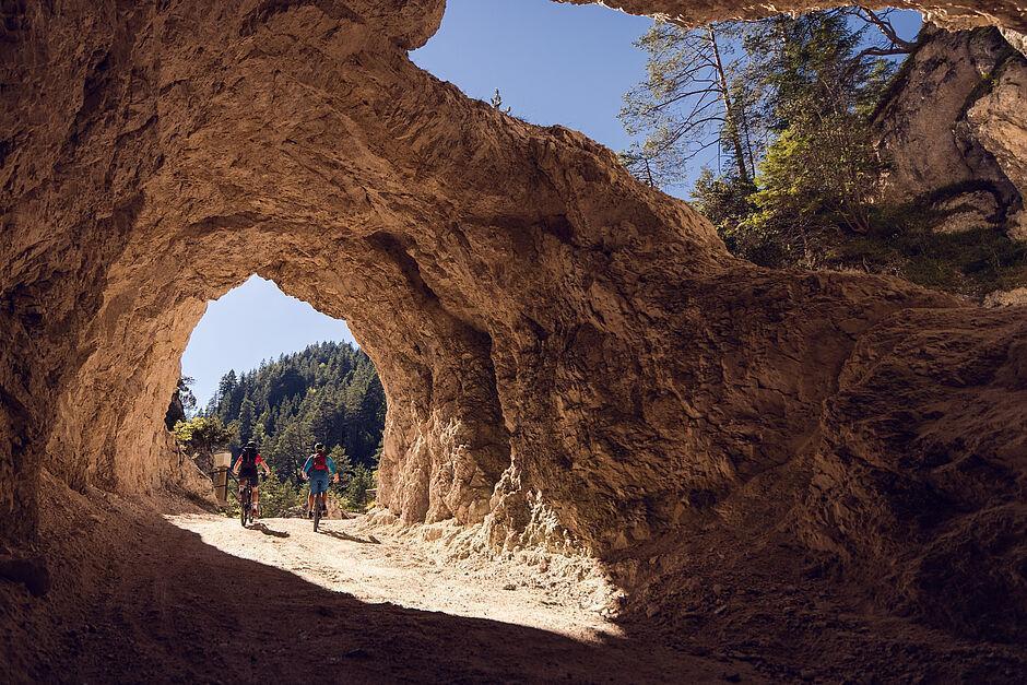 Zwei Radfahrer fahren durch einen natürlichen Steintunnel