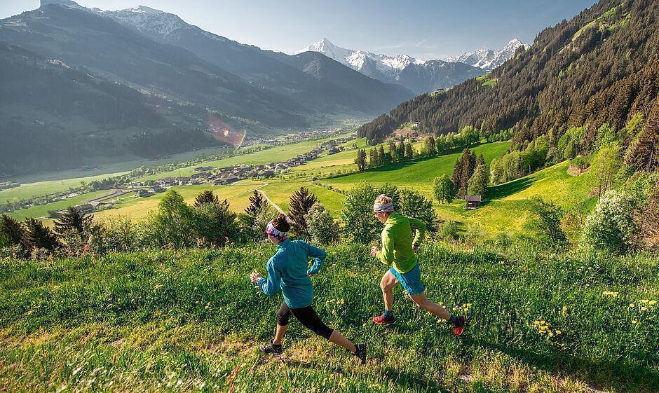 Zwei Jogger laufen auf einem Grasweg mit Blick auf das grüne Zillertal