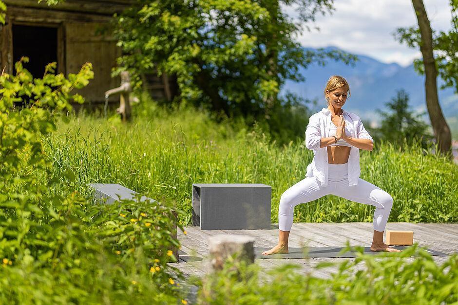 Hotelgast macht Yoga auf einem Holzsteg in der Natur des Wellness Hotel Tirol 