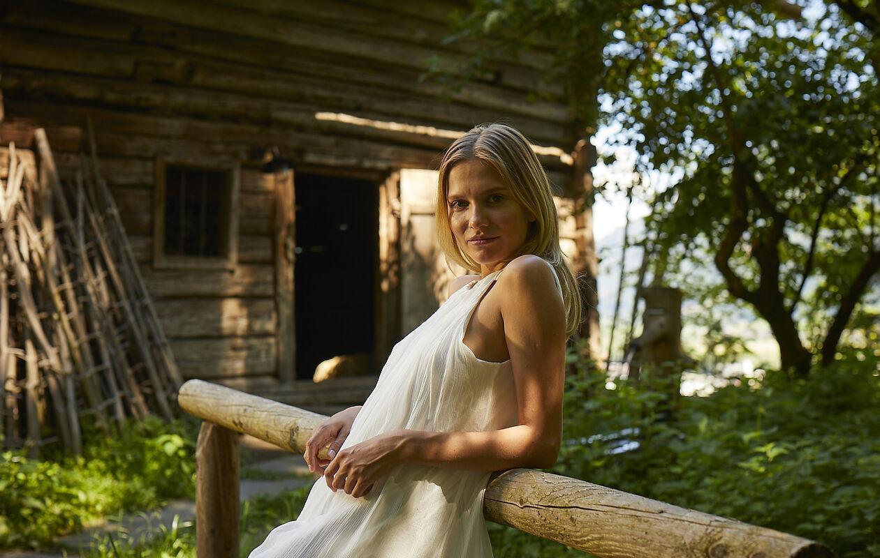 Dame posiert in weißem Kleid vor einer Holzhütte in der Natur in Tirol