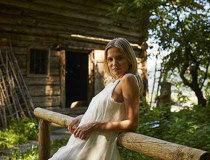 Dame posiert in weißem Kleid vor einer Holzhütte in der Natur in Tirol