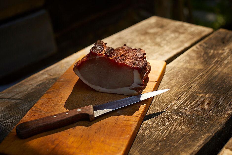 Brotzeitbrett mit Schinken auf einem Holztisch vor einer Hütte 