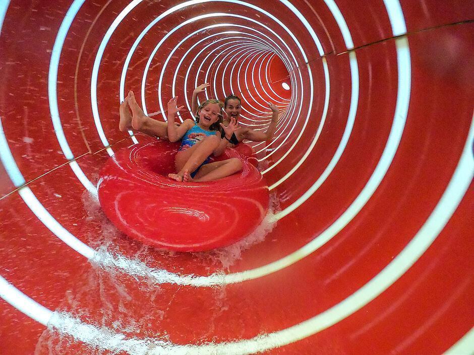 Mutter und Kind rutschen im Familienurlaub mit Schwimmring auf roter Wasserrutsche 