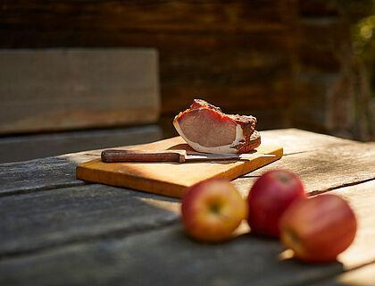 Brotzeitbrett mit Schinken und Äpfeln auf einem Holztisch im Freien 