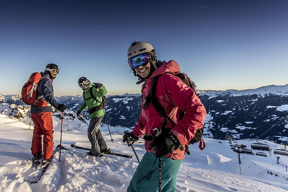 Eine Gruppe Skifahrer bereitet sich im Winterurlaub in Tirol lachend auf die Abfahrt vor und steht dabei vor einem winterlichen Bergpanorama