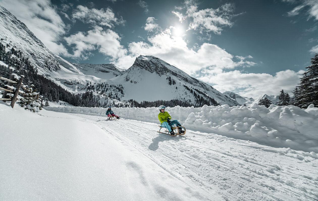 Kinder fahren Schlitten auf Rodelbahn in traumhafter Winterlandschaft in Tirol 
