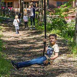 Kleiner Junge fährt im Familienurlaub glücklich auf einer Seilbahn im Wald 