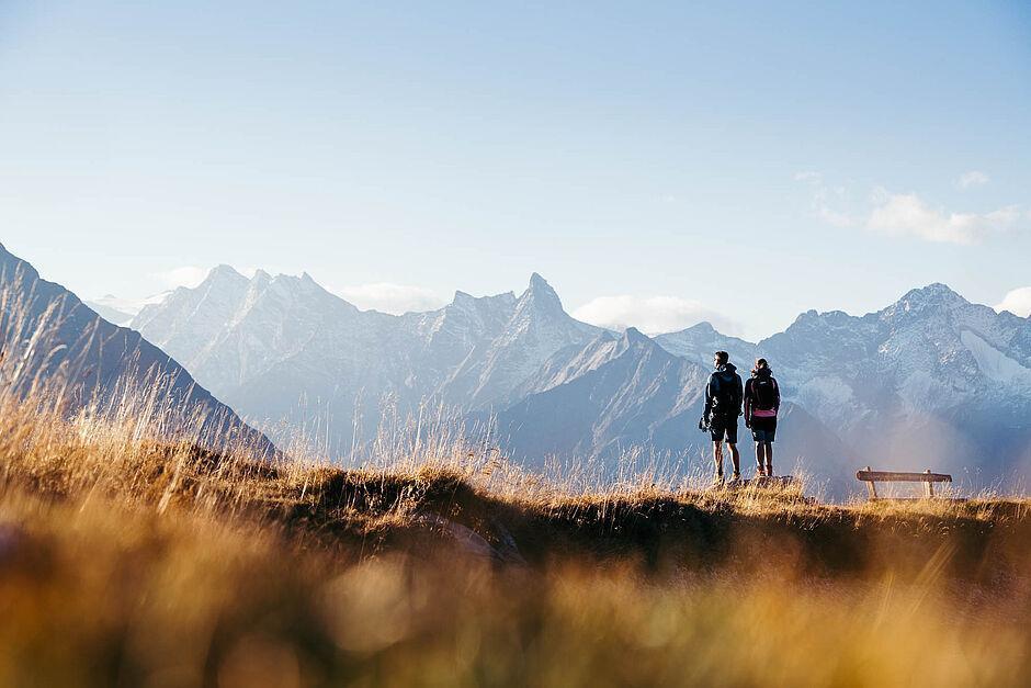 Ein Paar steht bei einem Wanderausflug im Sommerurlaub in Tirol auf einer Almwiese im Sonnenuntergang und genießt das atemberaubende Alpenpanorama