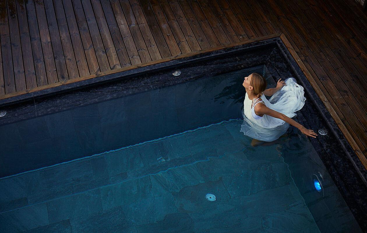 Eine Dame watet durch das klare Wasser des Infinity Pools auf dem Dach des Hotel Kaltenbach