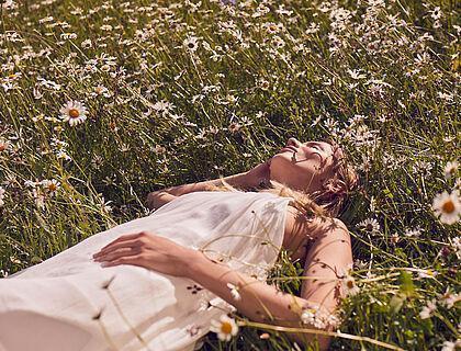 Dame im weißen Kleid liegt in einer Wiese mit zahlreichen Margeriten 