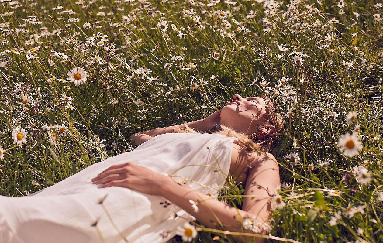 Dame im weißen Kleid liegt in einer Wiese mit zahlreichen Margeriten 