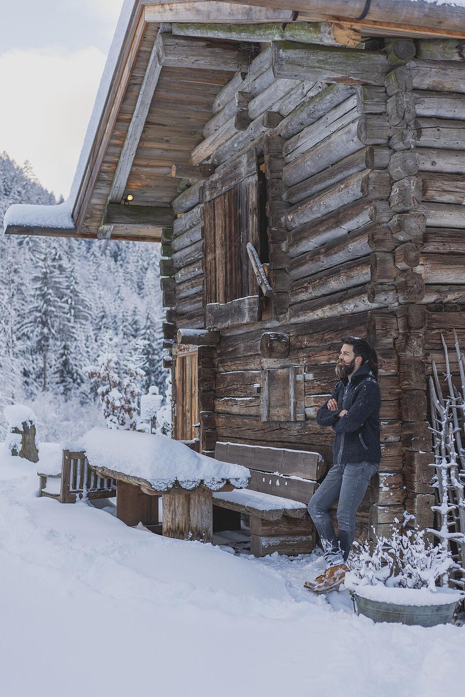 Mann lehnt an einer Holzhütte in den schneebedeckten Bergen von Tirol 