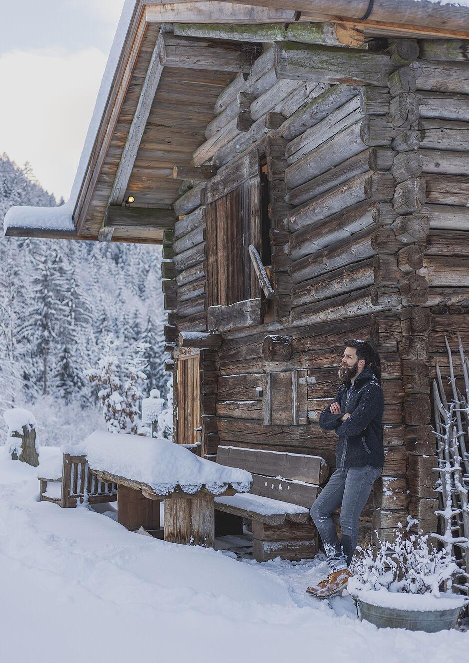 Mann lehnt an einer Holzhütte in den schneebedeckten Bergen von Tirol 