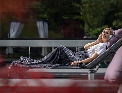 Hotelgast liegt auf einem Liegestuhl im Wellnesshotel Tirol und hört Musik 