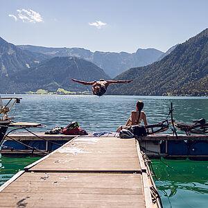 Mann springt von einem Holzsteg in den blauen Bergsee in Österreich 