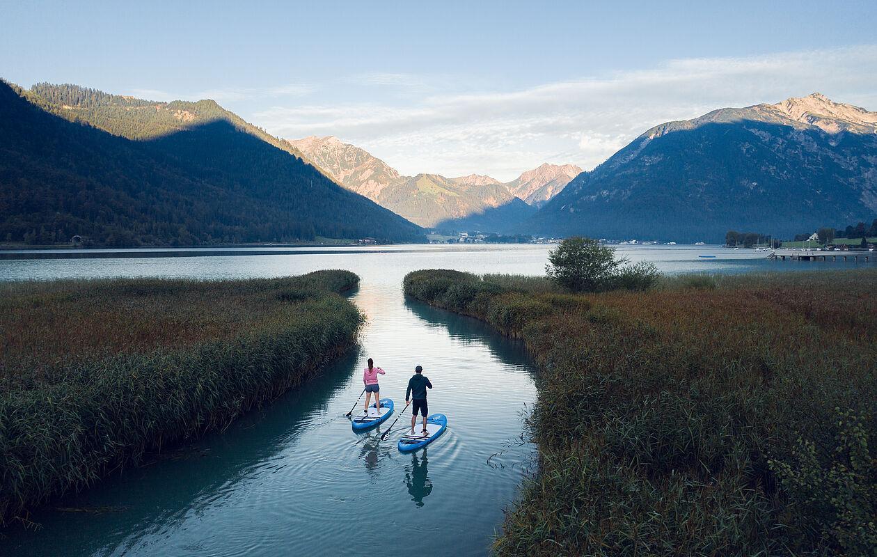 Paar fährt auf Stand-Up-Paddel-Boards über einen See nahe der Berge 