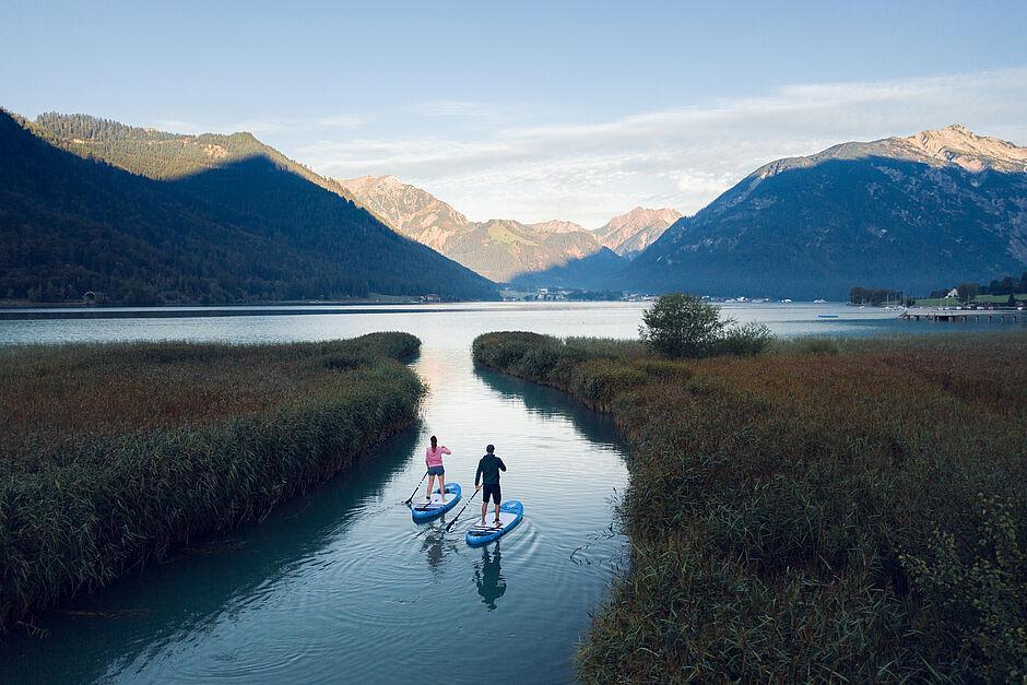 Ein Mann und eine Frau stehen auf Standup Paddles im Achensee