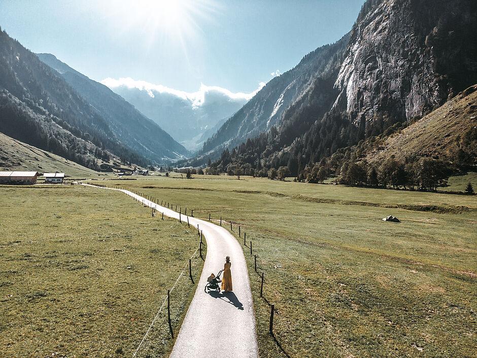 Eine Frau mit einem Baby im Kinderwagen vor Bergkulisse beim Urlaub in Tirol, Österreich